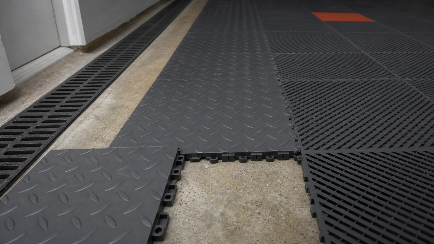 Graphite solid diamond-tread and open-grid garage tiles meeting over concrete with interlocking tabs exposed.